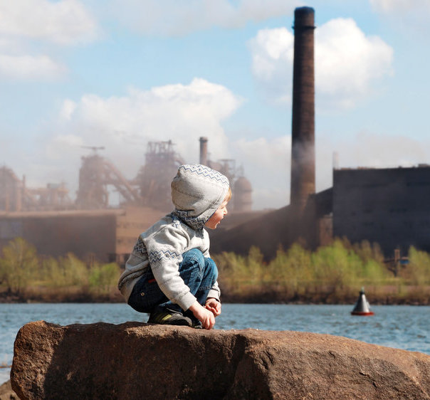 Playing little boy on the river coast in front of metallurgy plant